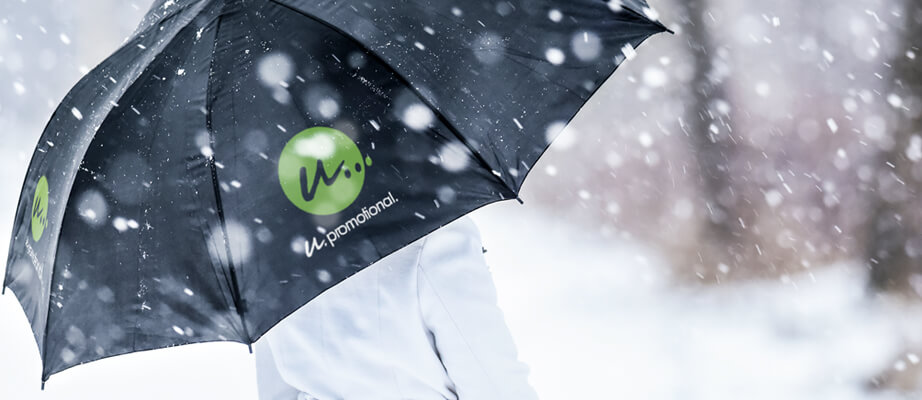 Frau steht im Regen mit schwarzem Regenschirm von Maxilia bedruckt mit Logo und Werbetext